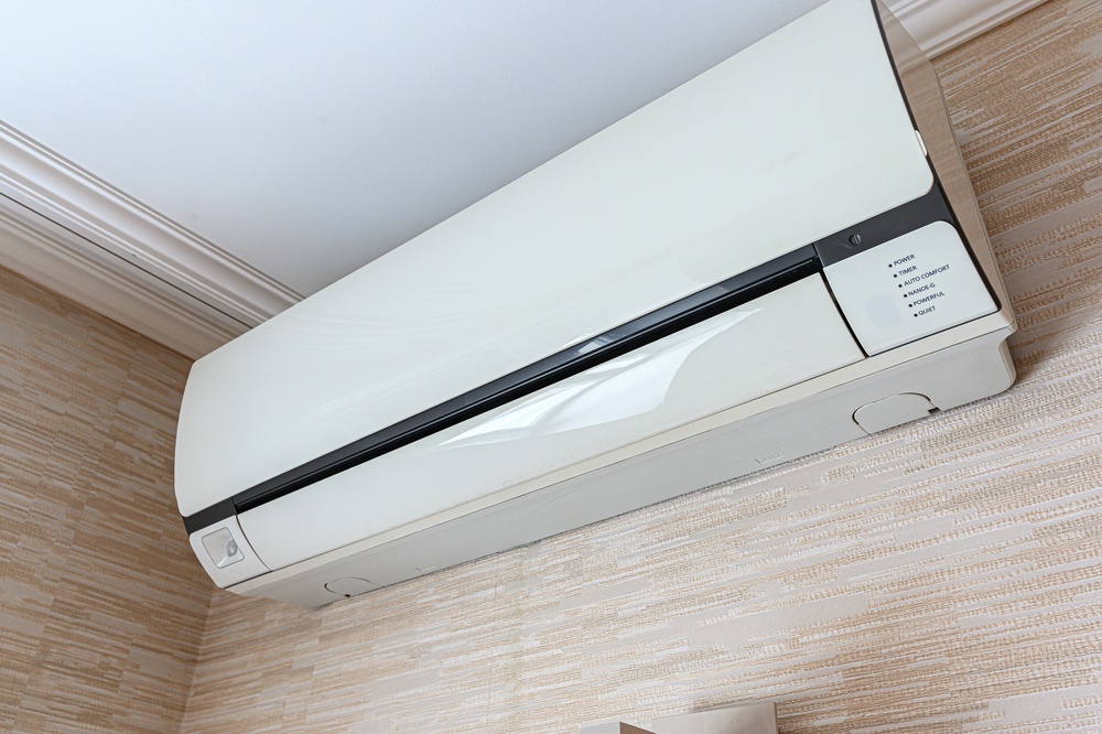 White wall-mounted ductless mini-split air conditioner near the ceiling of a room with beige textured walls